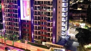 A multi-story building with a prominent illuminated sign on the facade, a flat roof, and a parking area in front. - City Apartment in Kingston AC with Pool (Kingston)