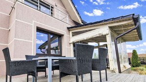 Une terrasse avec des meubles d’extérieur, un espace abrité et un bâtiment doté d’une fenêtre et d’un balcon.