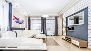 Un salon moderne avec un canapé d’angle, un téléviseur à écran plat et une grande fenêtre agrémentée de rideaux.