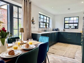 A modern kitchen with dark green cabinets, a dining area with a table set for breakfast, and large windows providing natural light. - Luxury/Hot tub/sauna/Sleeps 9/ Parking (Chepstow)