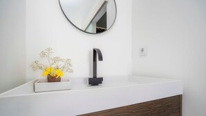 A modern bathroom with a white countertop, a black faucet, a round mirror, and a vase with yellow flowers. - Marina Legacy I Boutique Residence (Faro)