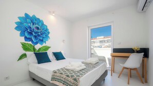 A modern bedroom with a large bed, a desk, and a view of buildings outside. - Marina Legacy I Boutique Residence (Faro)