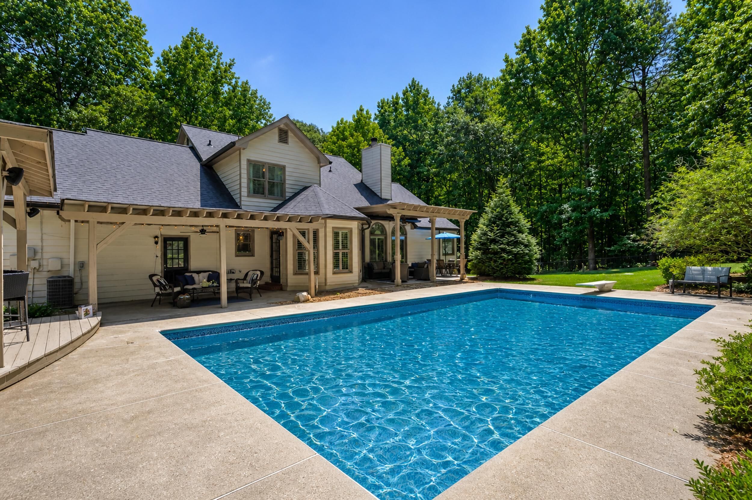 A house with a swimming pool, covered patio, and a lawn.