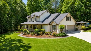 Een huis met twee verdiepingen, een overdekte veranda, een garage en een verzorgd gazon.