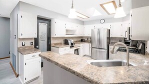 A modern kitchen with white cabinets, granite countertops, stainless steel appliances, and pendant lighting. - Up to Par in Hot Springs Village, AR (Hot Springs Village)