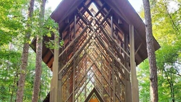 A large, modern building with a wooden facade and a central wooden door, surrounded by trees. - Up to Par in Hot Springs Village, AR (Hot Springs Village)