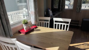 Ruokailutilassa on puinen pöytä ja valkoiset tuolit, ruukussa oleva kasvi sekä ikkuna, josta on näkymä rakennuksiin.
