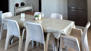 A dining area with a table set for four, white chairs, a hanging light fixture, and a wardrobe. - OASIS 360° Apartment (Kos)