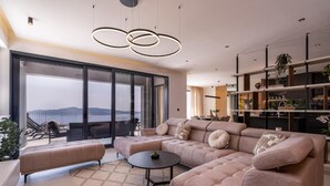 Uma sala de estar ampla com um sofá seccional grande, uma mesa de centro redonda e vista para o exterior.