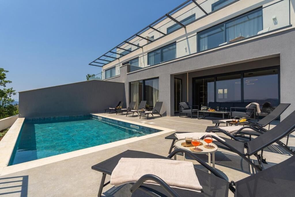 A modern building with a rooftop pool, lounge chairs, and a dining area.