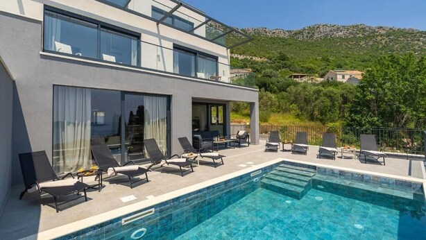 Um hotel moderno com piscina no terraço, espreguiçadeiras e vista para a paisagem ao redor.