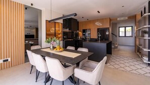 Uma cozinha moderna com ilha central, área de refeições com mesa e cadeiras, e escada que leva a outro andar.