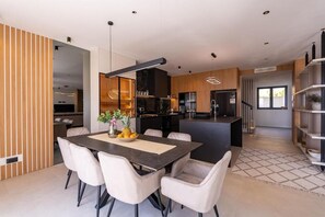 A modern kitchen with a central island, a dining area with a table and chairs, and a staircase leading to another level. - Green Sunrise Villa - Stunning Sea View Villa with Private Pool near Dubrovnik (Brsečine)