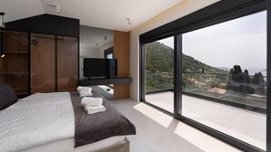 Quarto moderno com uma cama grande, televisão e varanda com vista para a cidade.