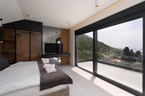 A modern bedroom with a large bed, a TV, and a balcony with a city view. - Green Sunrise Villa - Stunning Sea View Villa with Private Pool near Dubrovnik (Brsečine)