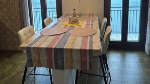 A dining area with a table set for four, a chandelier, and large windows with a view of a body of water and mountains. - House of sails in the bay of sails (Valmadrera)