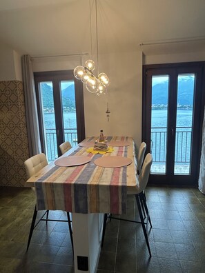 Ein Essbereich mit einem Tisch für vier Personen, einer Chandelüster und großen Fenstern mit Blick auf ein Gewässer und Berge.