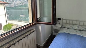 A bedroom with a bed, a window with a view of a body of water and mountains, a radiator, and a bedside table. - House of sails in the bay of sails (Valmadrera)