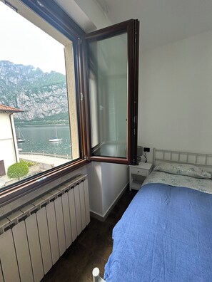 Ein Schlafzimmer mit Bett, einem Fenster mit Blick auf ein Gewässer und Berge, einem Heizkörper und einem Nachttisch.