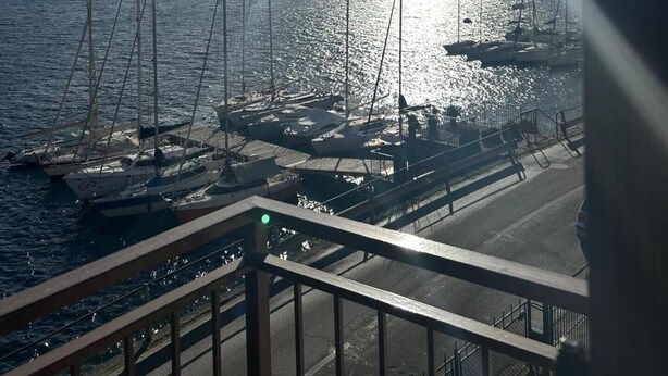 A marina with sailboats docked, a clear sky, and mountains in the background. - House of sails in the bay of sails (Valmadrera)