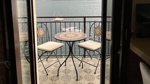 A balcony with a view of a body of water and mountains, featuring a round table and two chairs. - House of sails in the bay of sails (Valmadrera)