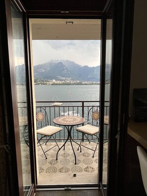 Ein Balkon mit Blick auf ein Gewässer und Berge, ausgestattet mit einem runden Tisch und zwei Stühlen.