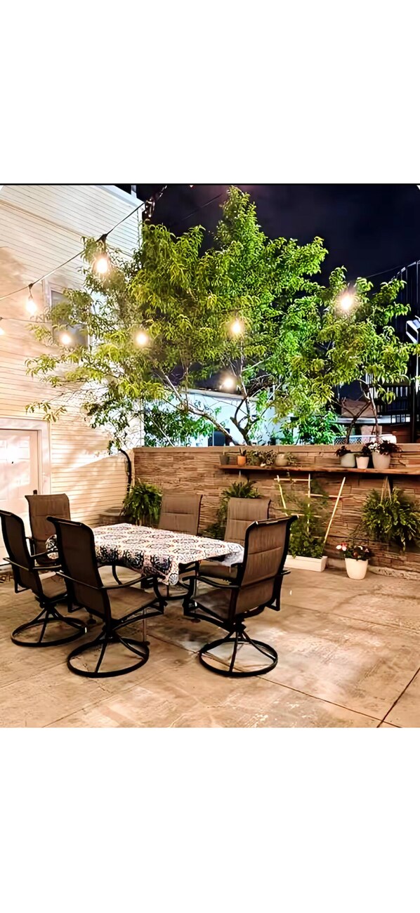 An outdoor patio with a table and chairs, string lights, and potted plants.