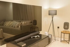 A modern living room with a sofa, a coffee table, a TV, a floor lamp, and a speaker. - Luxury Apartment in Makkah (Makkah)