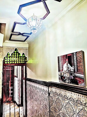 Una escalera con detalles en azulejos, un candelabro y un cuadro de una persona.