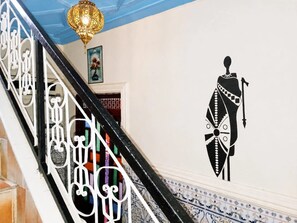 A staircase with ornate metal railings and a wall mural of a figure in traditional attire. - Entire Traditional Riad - Not Shared - Medina Center - Patio  ROOFTOP (Marrakesh)