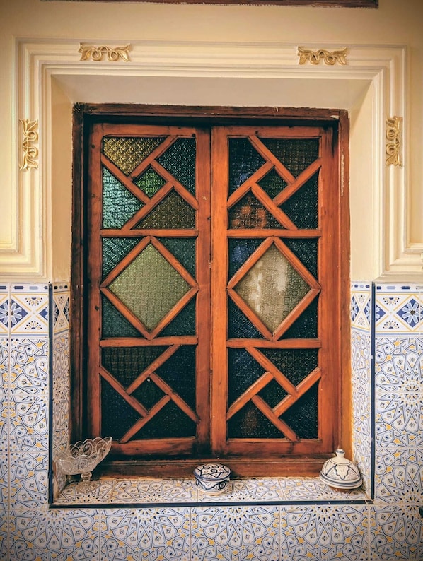 Una ventana con un diseño geométrico y un pequeño estante con un cuenco decorativo y un recipiente.