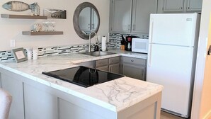 A modern kitchen with a central island, grey cabinets, a white refrigerator, and a microwave.