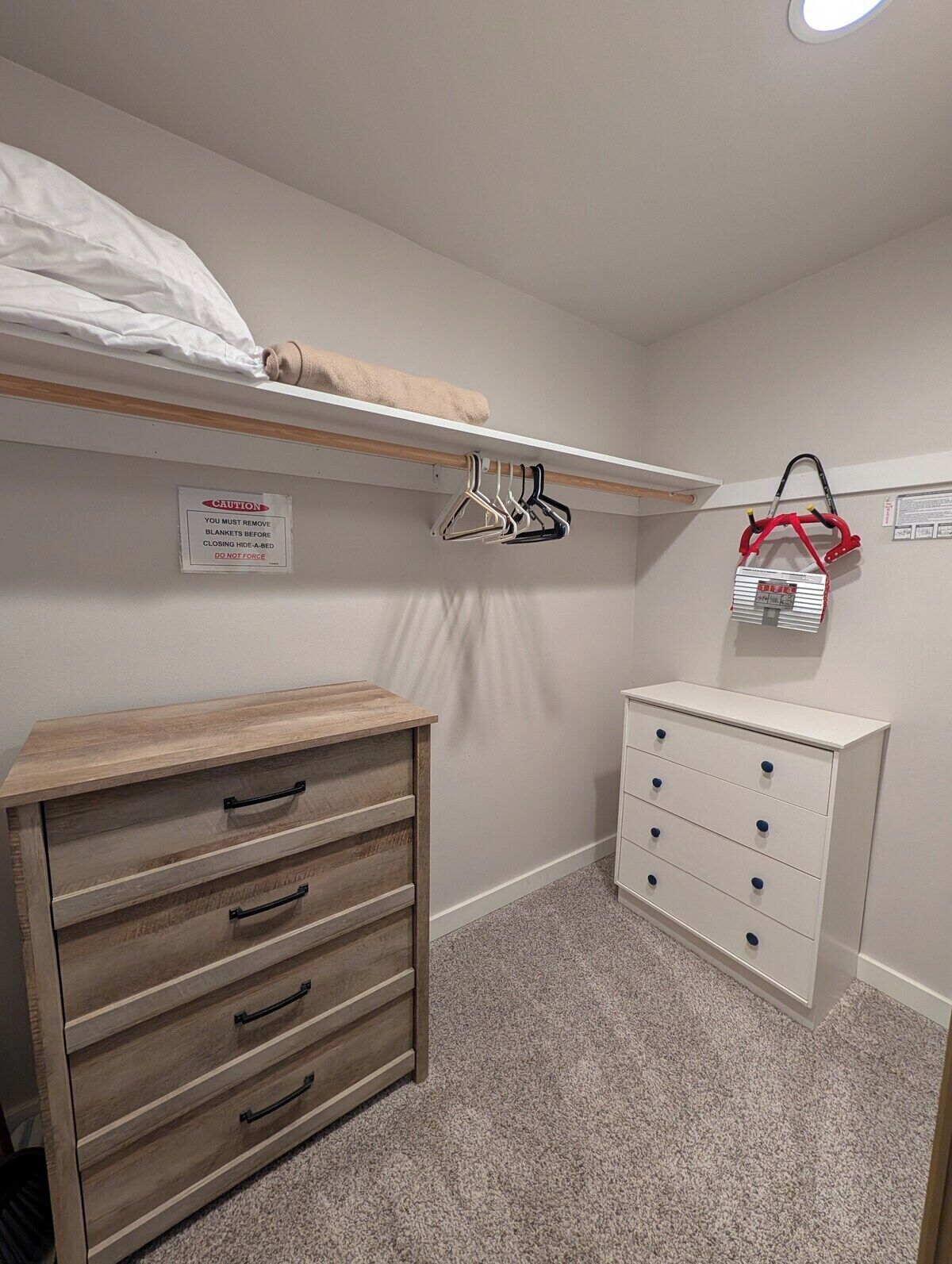 A small, neatly organized bedroom with a bunk bed, a wooden dresser, a white chest of drawers, and a hanging clothes rack.