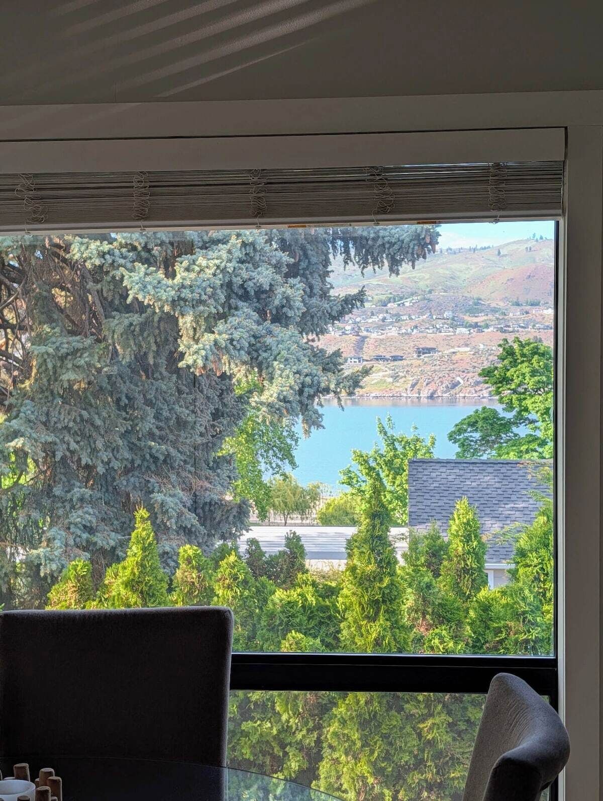 A room with a large window overlooking a lake and a hilly landscape.