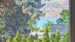 A room with a large window overlooking a lake and a hilly landscape.