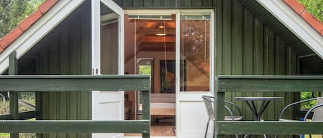 A wooden cabin with a sloped roof, a deck with chairs, and a glass door leading inside.