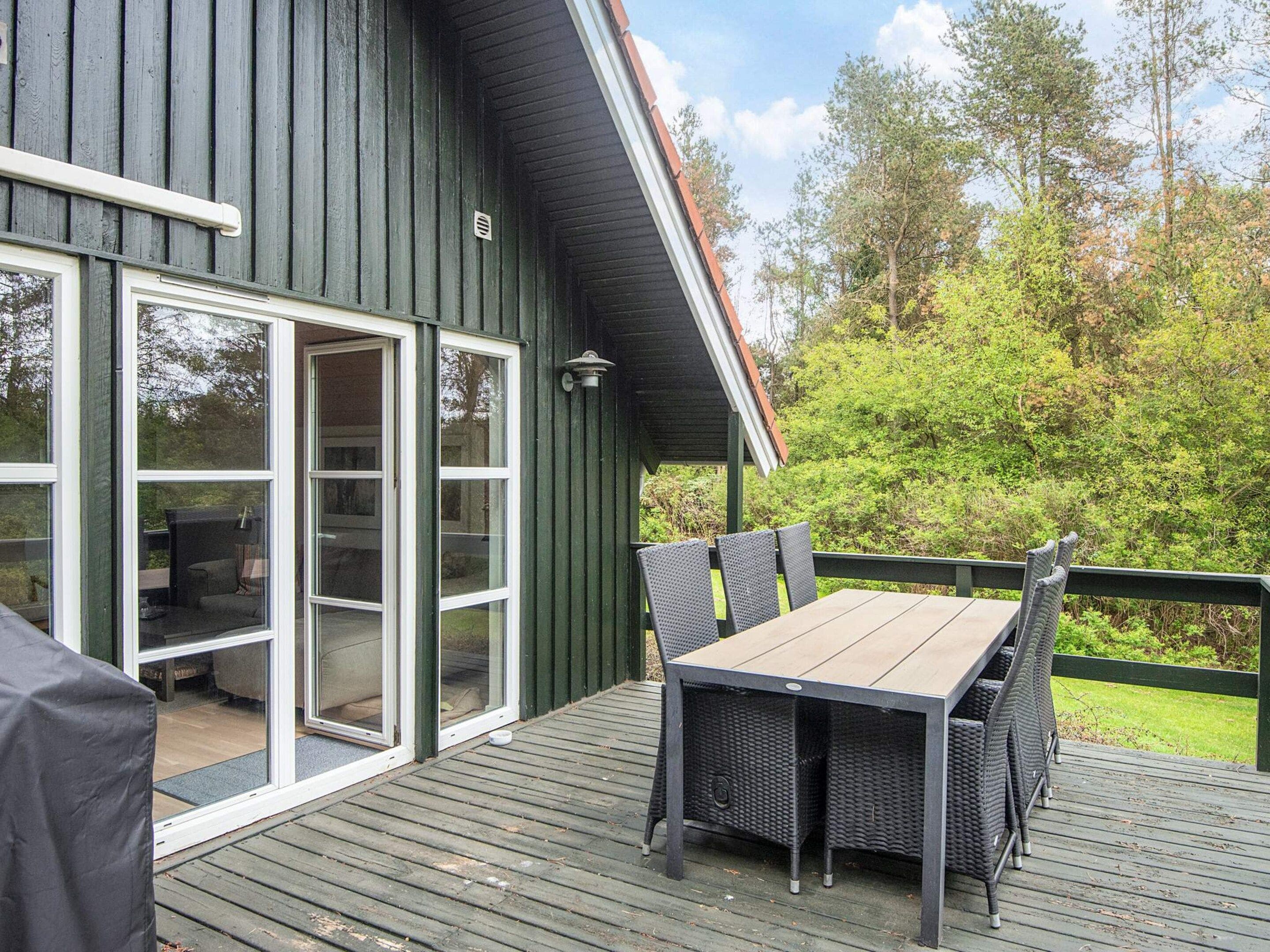 Une terrasse dotée d’une table et de chaises, d’un espace extérieur couvert aménagé en coin salon, et d’une grande porte-fenêtre coulissante donnant accès à un espace intérieur.