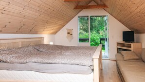 Une chambre avec un plafond en pente, un lit, un canapé, une télévision et une vue sur la verdure à l’extérieur.