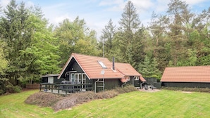 Une cabane avec un toit en pente, une cheminée et une terrasse dotée de meubles pour se détendre à l’extérieur.