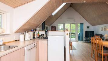 Cocina con refrigerador, pileta y muebles de madera. Hay un comedor con sillas y una mesa.