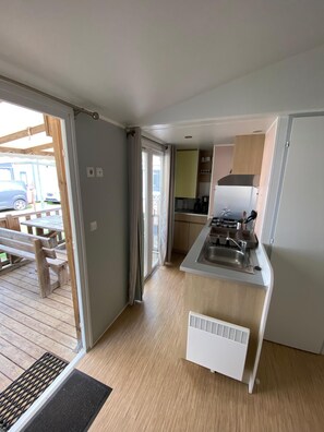 Eine kompakte Küche mit eingebautem Herd, Spüle und Kühlschrank. Vor der Tür befindet sich ein Holzdeck.