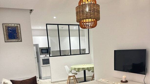 Un salon moderne avec un canapé, une table basse en verre, un téléviseur et un luminaire suspendu.