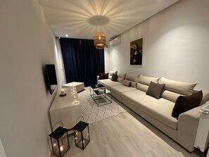 A modern living room with a sofa, a coffee table, a TV, and a painting on the wall. - Charming apartment in the heart of La Marsa - Near beach, Carthage & Tunis (La Marsa)