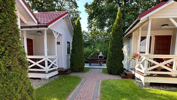 A pathway leading to two white cabins with red roofs, surrounded by greenery and a brick path. - Ferien Bobolin Ferienhäuser by Interhome (Dabki)