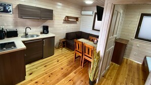 A compact kitchen with a sink, toaster, and coffee maker, a dining area with a table and chairs, and a potted plant. - Ferien Bobolin Ferienhäuser by Interhome (Dabki)