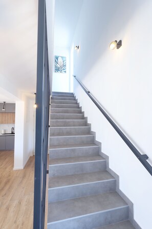 A staircase with a handrail, a light fixture on the wall, and a view of a kitchen area. - 3-bedroom villa in gorgeous Zaton with cool AC (Zaton)
