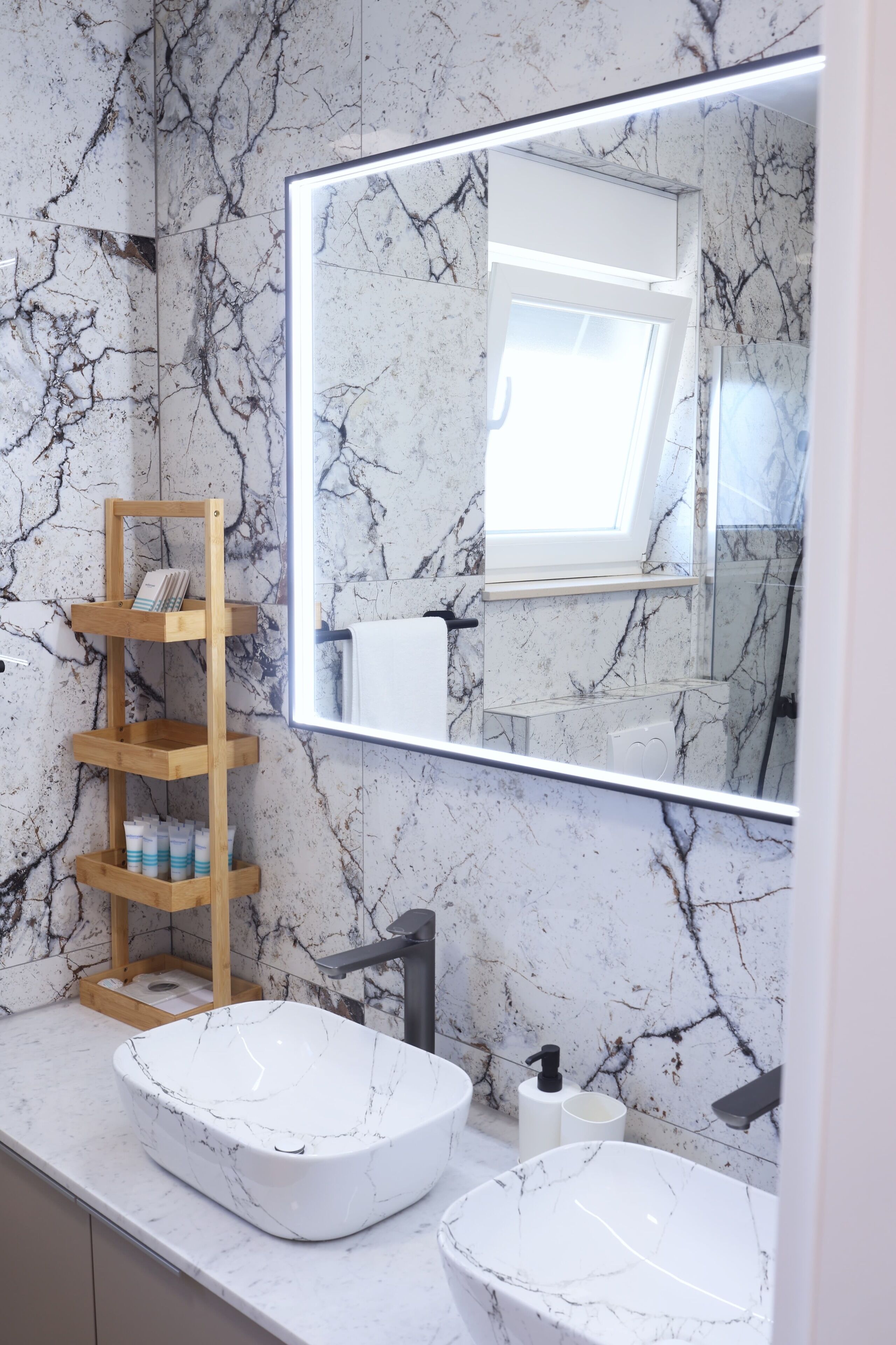 Un bagno con schienale in marmo, mobile contenitore in legno, due lavabi e uno specchio grande.