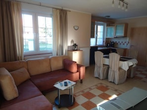 Un salon avec un canapé, une petite table sur laquelle se trouve un ordinateur portable, un coin cuisine avec une table à manger et des chaises, et une fenêtre avec des rideaux.