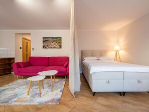 A room with a bed, a red sofa, a small table, and a lamp.