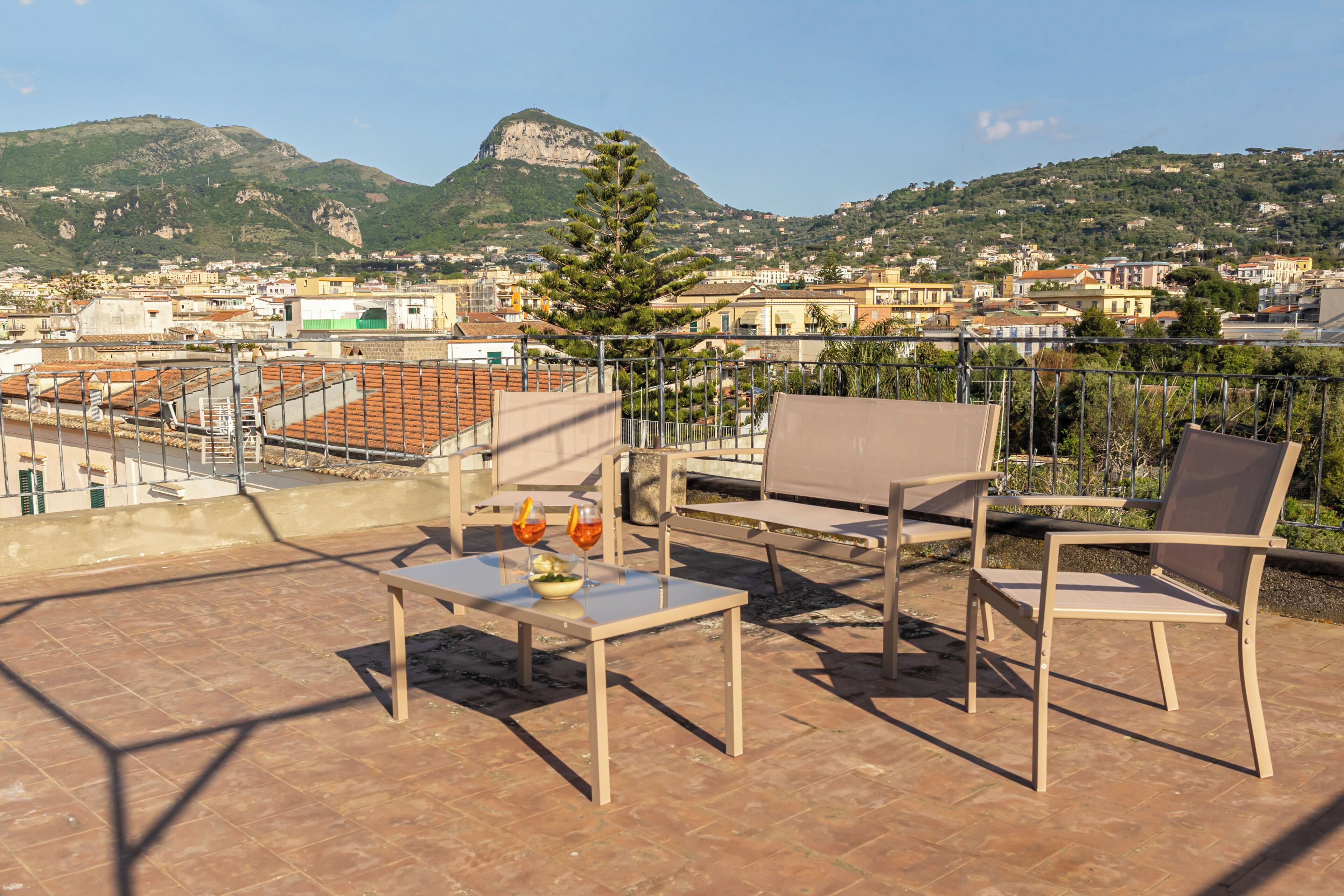 Une terrasse aménagée avec du mobilier d’extérieur, une table avec des verres et une vue sur un paysage urbain, avec des montagnes en arrière-plan.